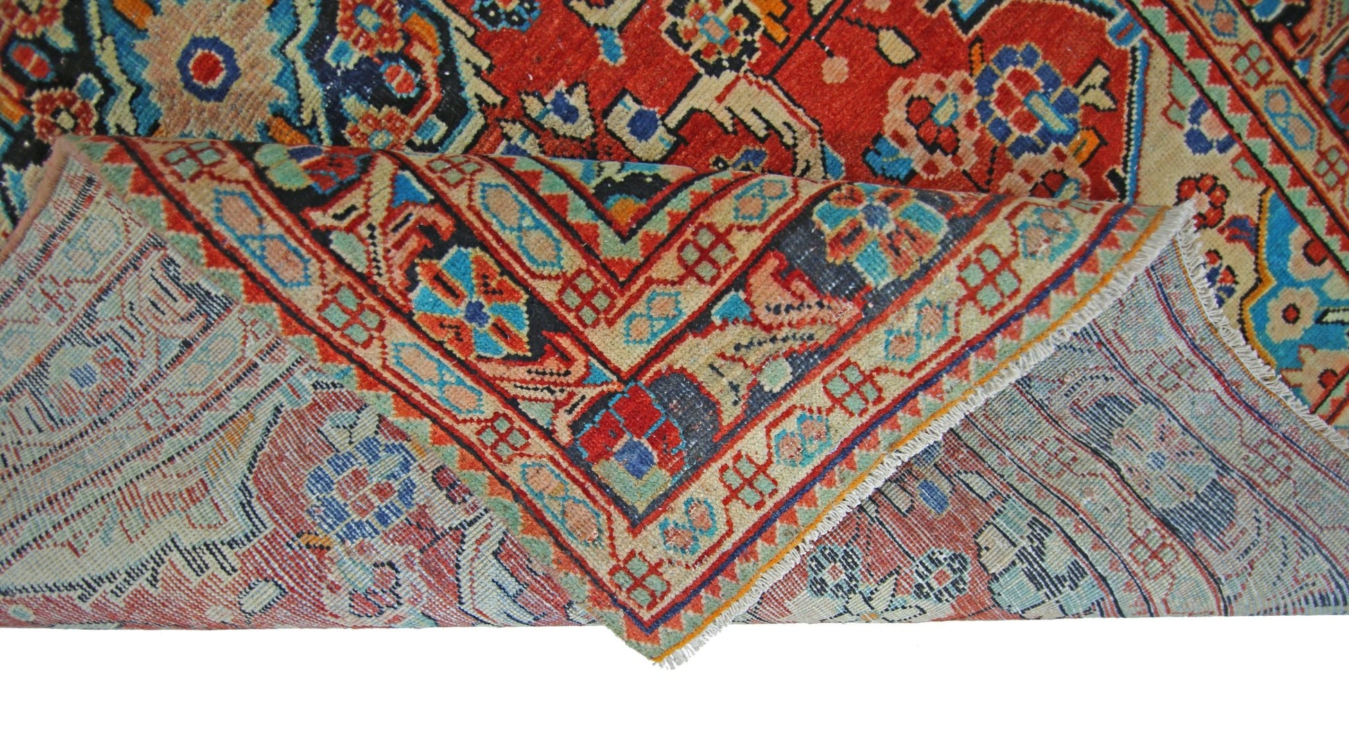 A vintage Persian Tabriz rug with a folded corner showing its intricate red and blue floral pattern.