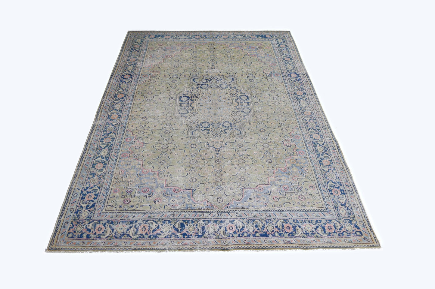 A vintage Persian Tabriz rug featuring a central blue medallion on a faded green field.