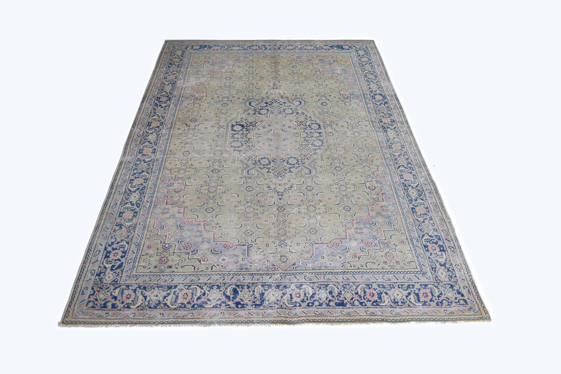 A vintage Persian Tabriz rug featuring a central blue medallion on a faded green field.