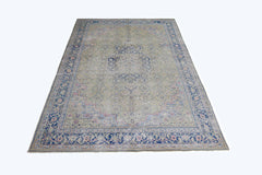 A vintage Persian Tabriz rug featuring a central blue medallion on a faded green field.