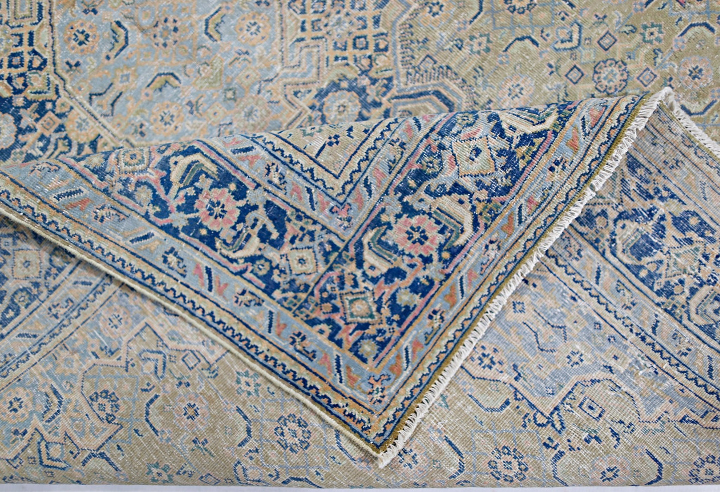 A vintage Persian Tabriz rug featuring intricate blue, pink, and beige floral patterns.