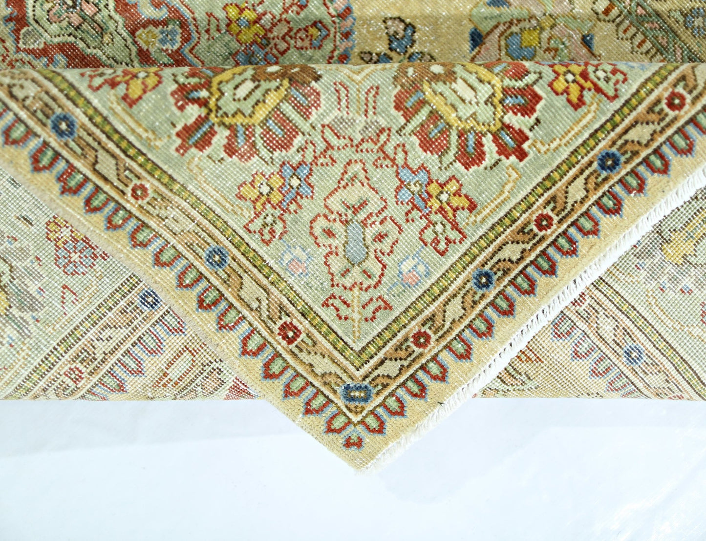 A corner of a vintage Persian Tabriz rug showing intricate floral patterns in red, blue, and gold.