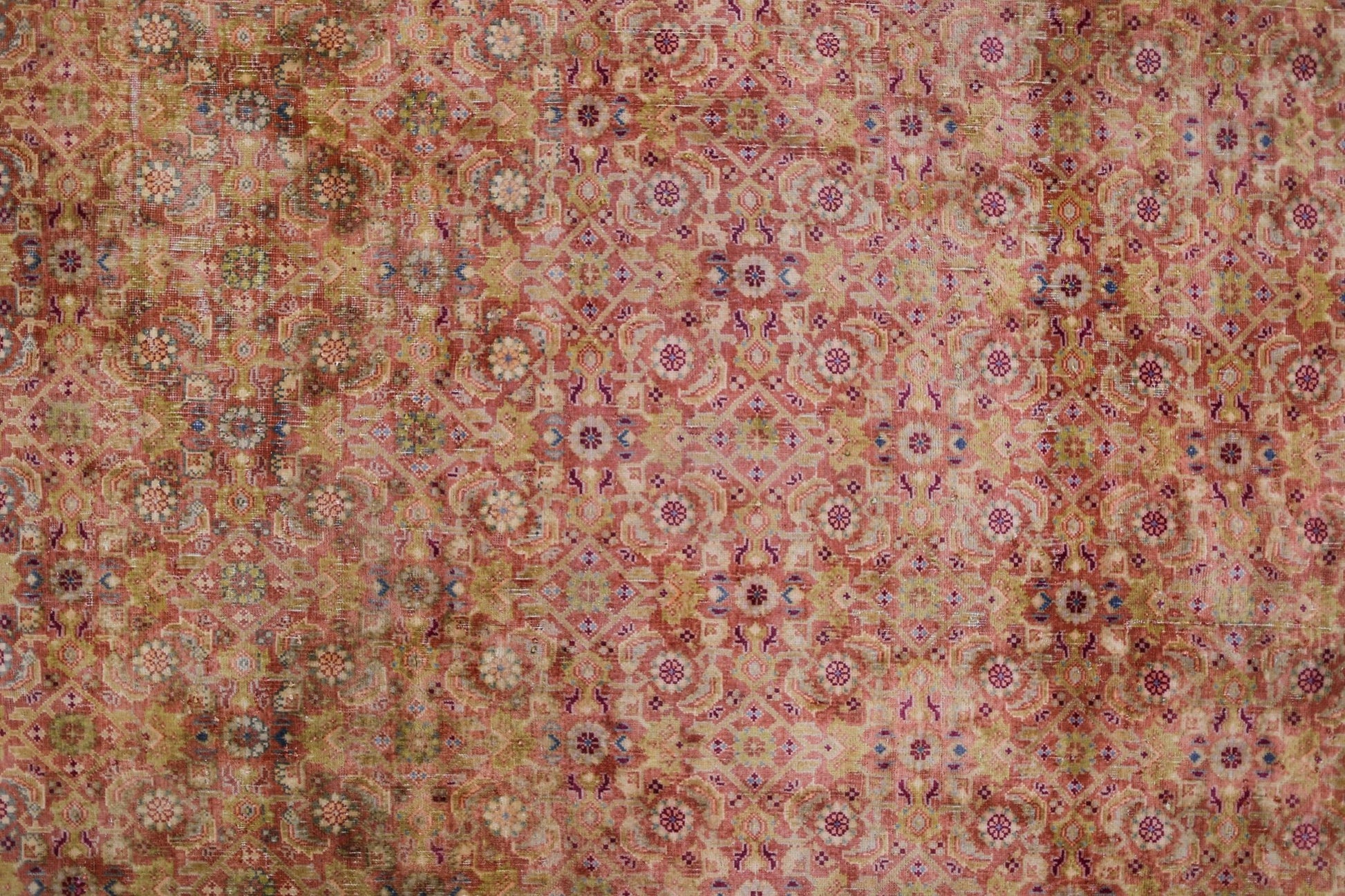 A vintage Persian Tabriz rug featuring an intricate, faded floral pattern in shades of red and gold.