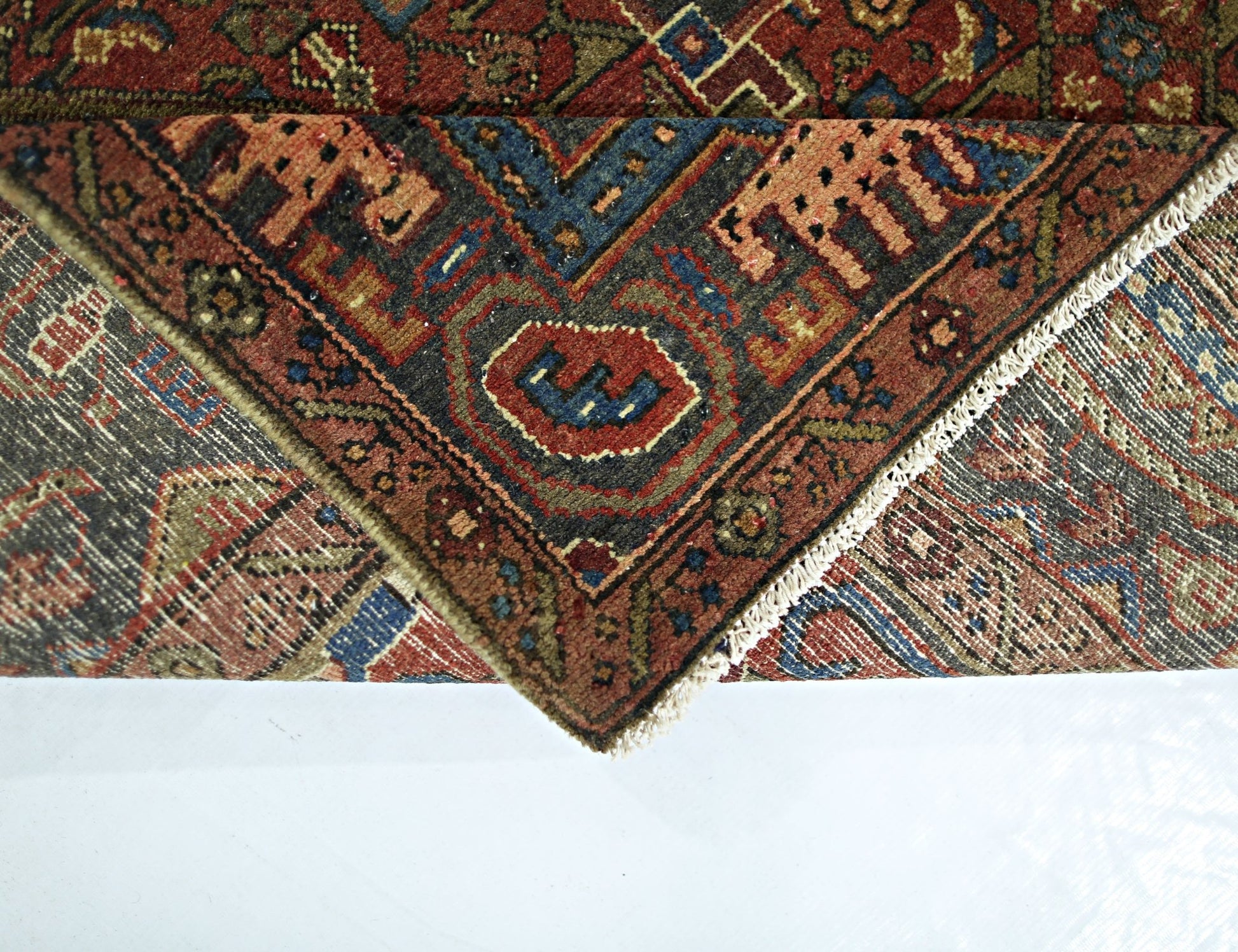 A folded vintage Persian Tabriz rug featuring intricate geometric patterns in red, blue, and brown.