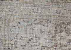 A close-up of a vintage Persian Kerman rug featuring intricate floral patterns in neutral tones.