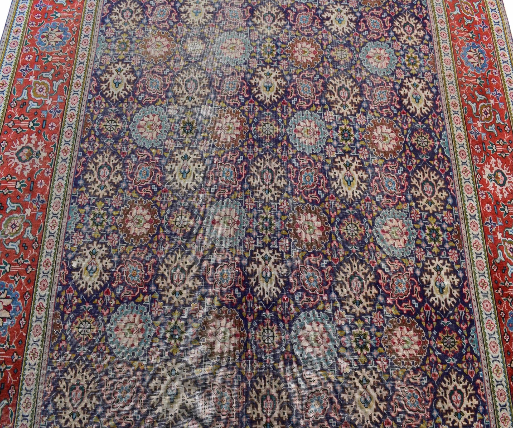 A vintage handwoven Persian Tabriz rug featuring a dense floral pattern in blue and red tones.