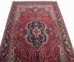 A vintage Persian Tabriz rug featuring a central medallion and intricate floral patterns in red.