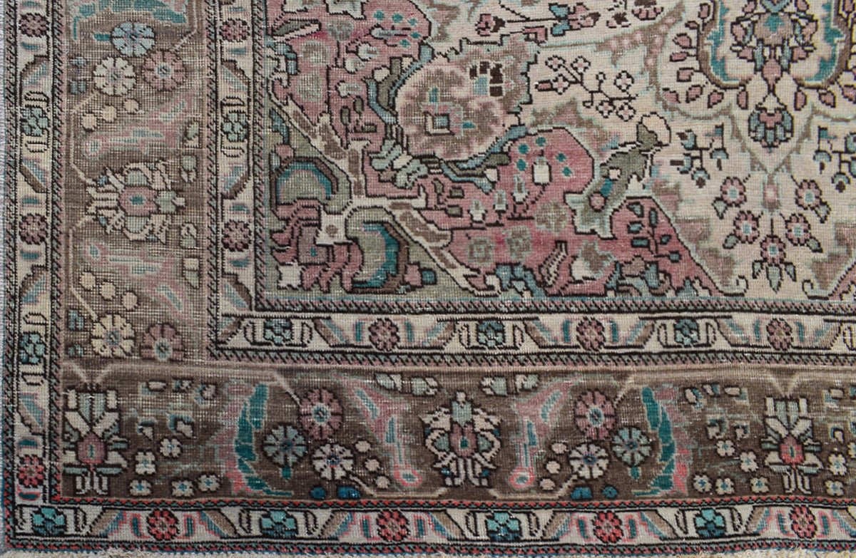 A vintage Persian Tabriz rug featuring intricate floral patterns in muted pink, blue, and brown.