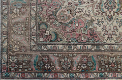 A vintage Persian Tabriz rug featuring intricate floral patterns in muted pink, blue, and brown.