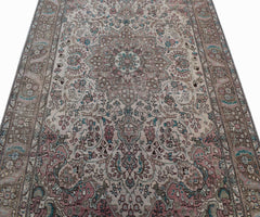 A vintage handwoven Persian Tabriz rug featuring intricate floral patterns in muted pink and blue.