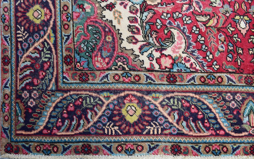 A close-up of a vintage Persian Tabriz rug featuring intricate floral patterns and a deep red border.