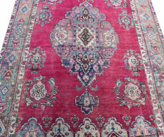 A vintage Persian Tabriz rug featuring a central medallion and intricate floral patterns in shades of pink and blue.