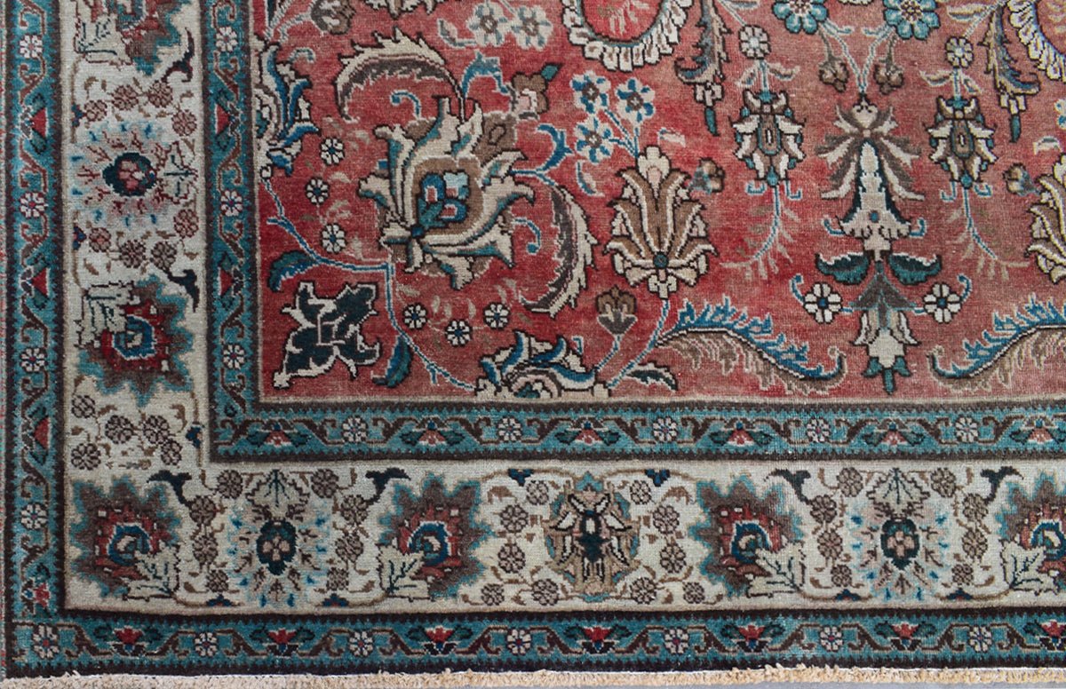 A vintage Persian Tabriz rug featuring an intricate floral pattern in red, blue, and cream tones.