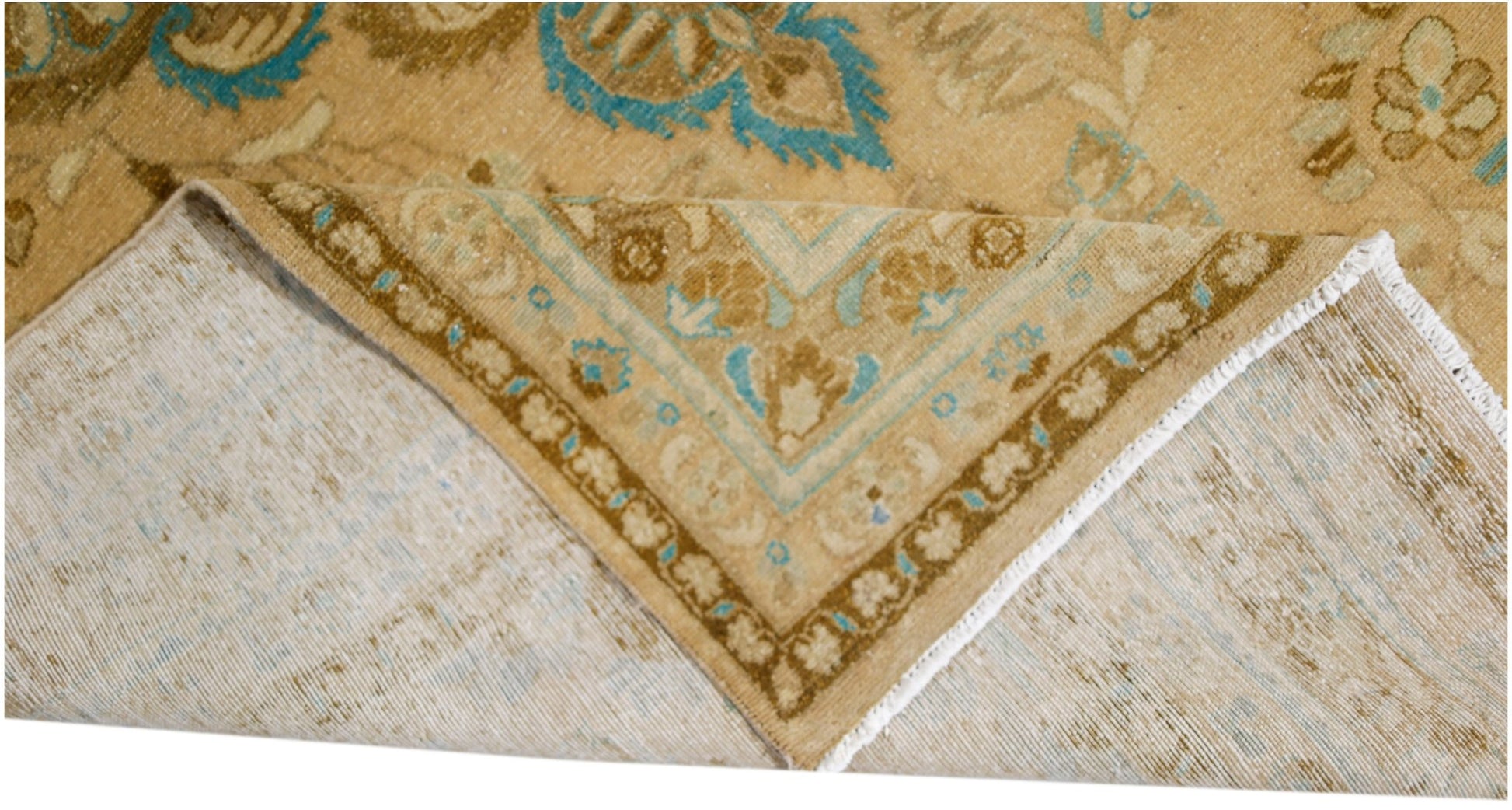 A vintage Persian Tabriz rug with a tan and blue floral pattern, shown folded to reveal its back.