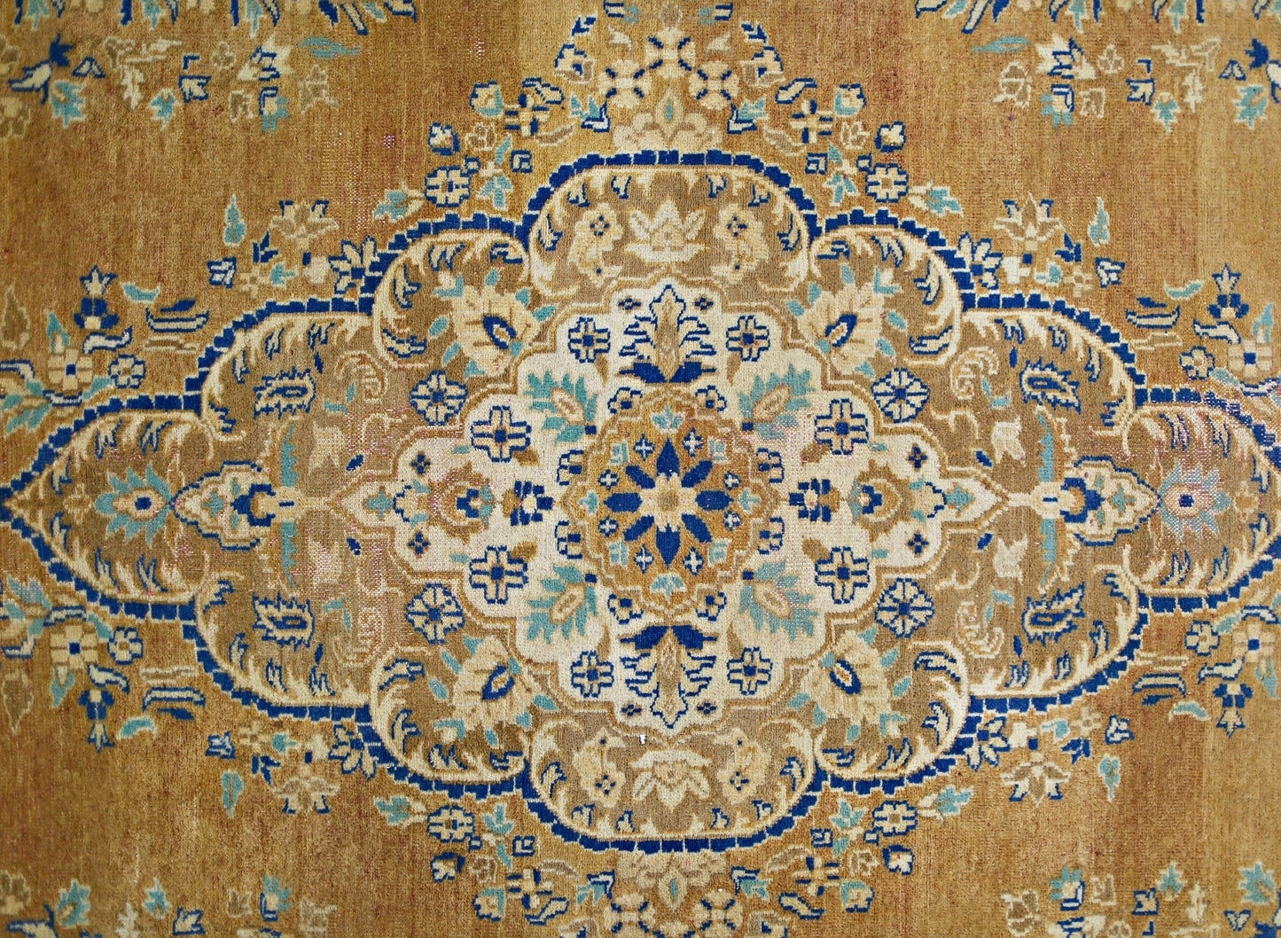 A vintage Persian Tabriz rug featuring an intricate blue and cream floral medallion on a tan field.