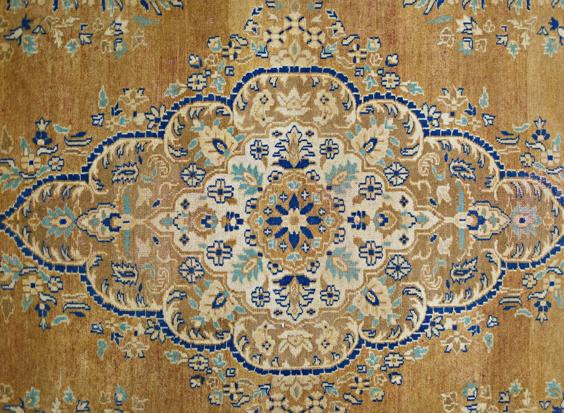 A vintage Persian Tabriz rug featuring an intricate blue and cream floral medallion on a tan field.
