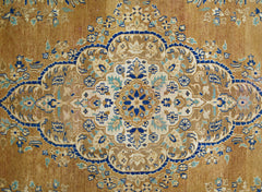 A vintage Persian Tabriz rug featuring an intricate blue and cream floral medallion on a tan field.