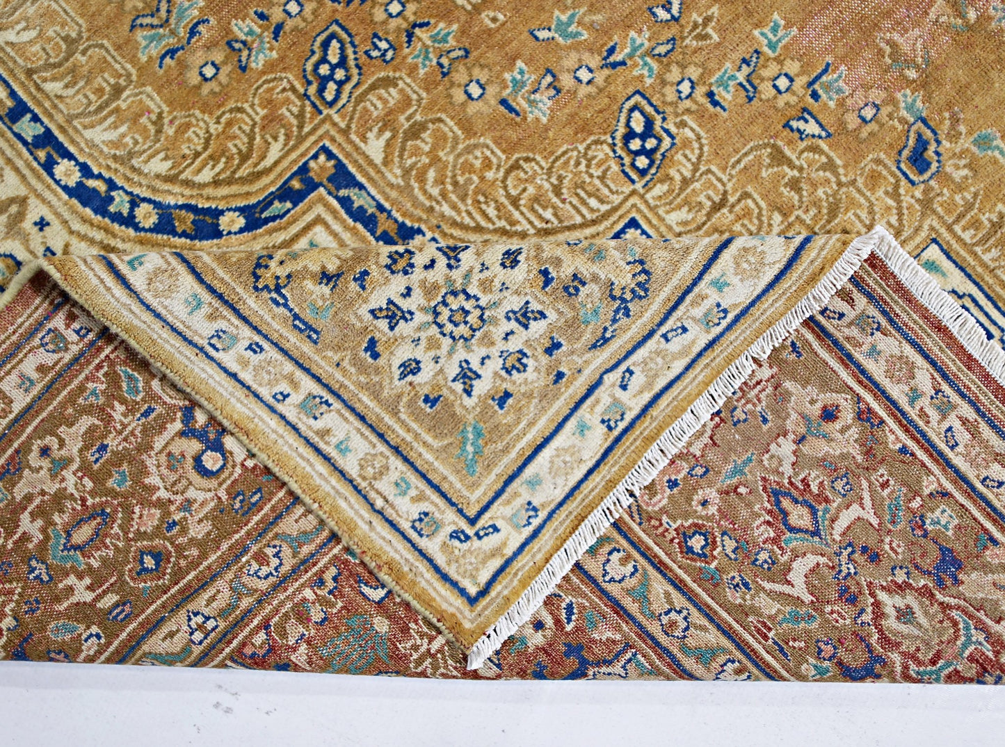 A vintage Persian Tabriz rug with intricate floral patterns in blue, gold, and red tones.