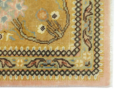 A corner detail of a vintage Persian Tabriz rug featuring intricate floral patterns in gold, pink, and green.