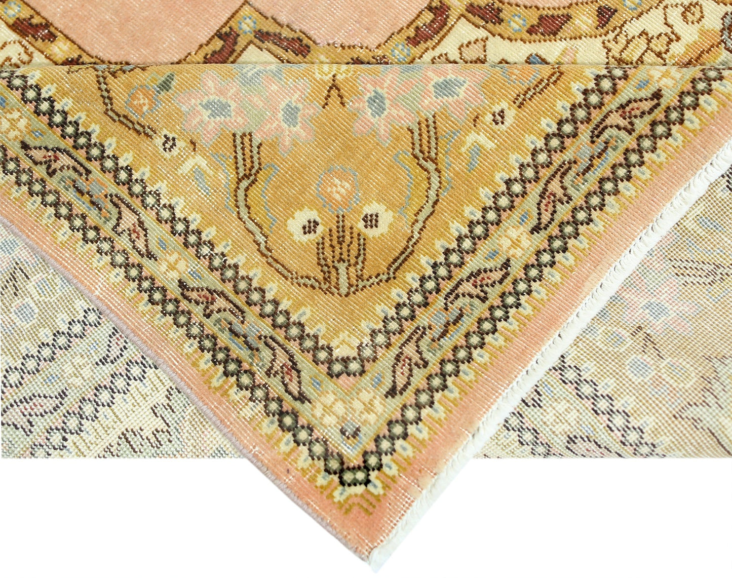 A corner of a vintage Persian Tabriz rug showing intricate floral patterns in peach and gold.