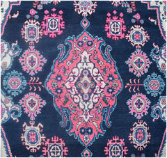 A vintage Persian Tabriz rug featuring a central pink medallion on a dark blue field.