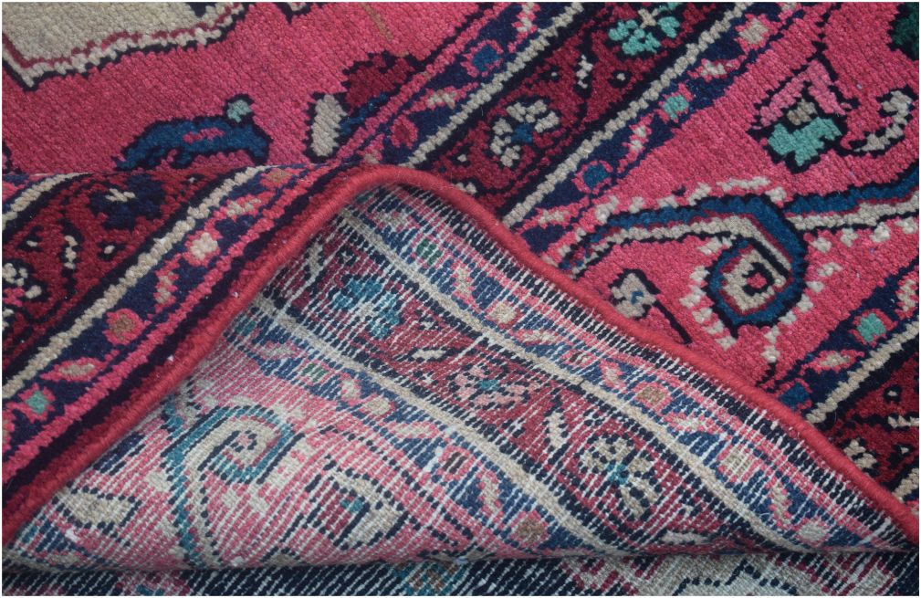 A corner of a vintage Persian Tabriz rug is folded back to reveal its hand-knotted wool construction.