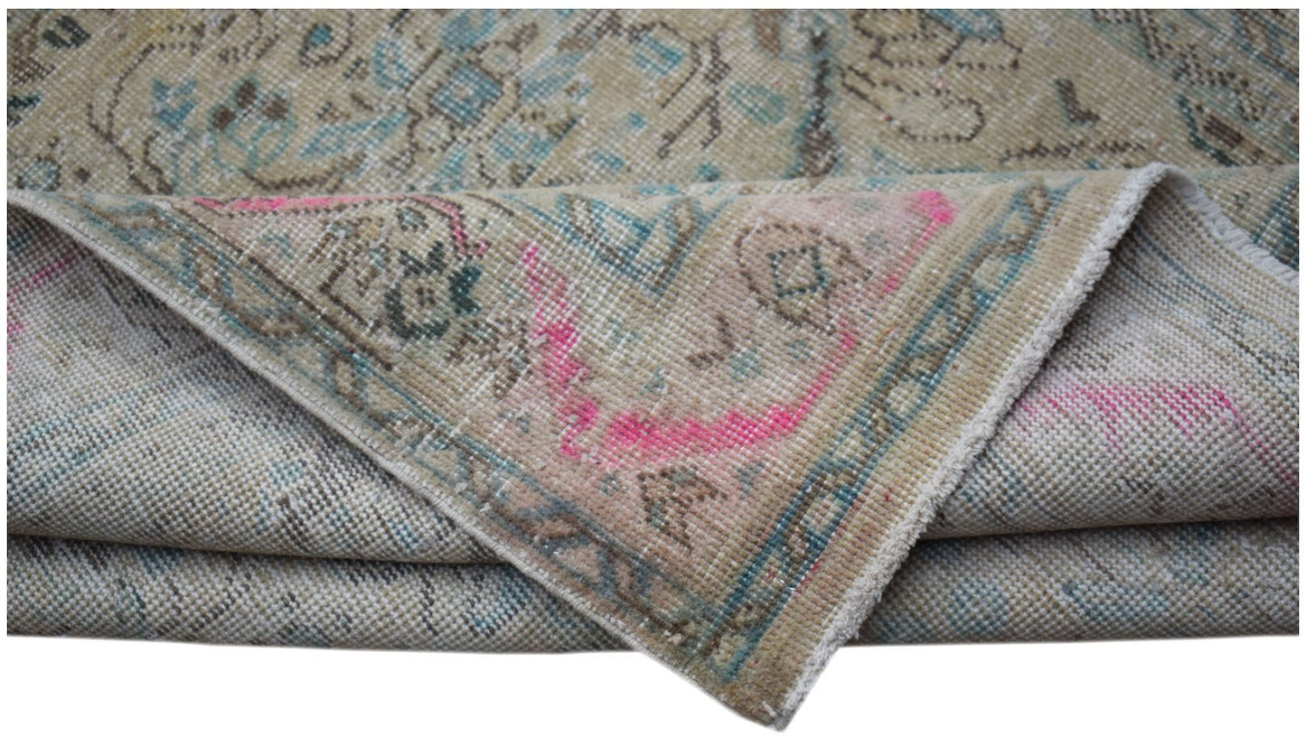 A folded vintage Persian Tabriz rug featuring a faded floral pattern in beige, blue, and pink.