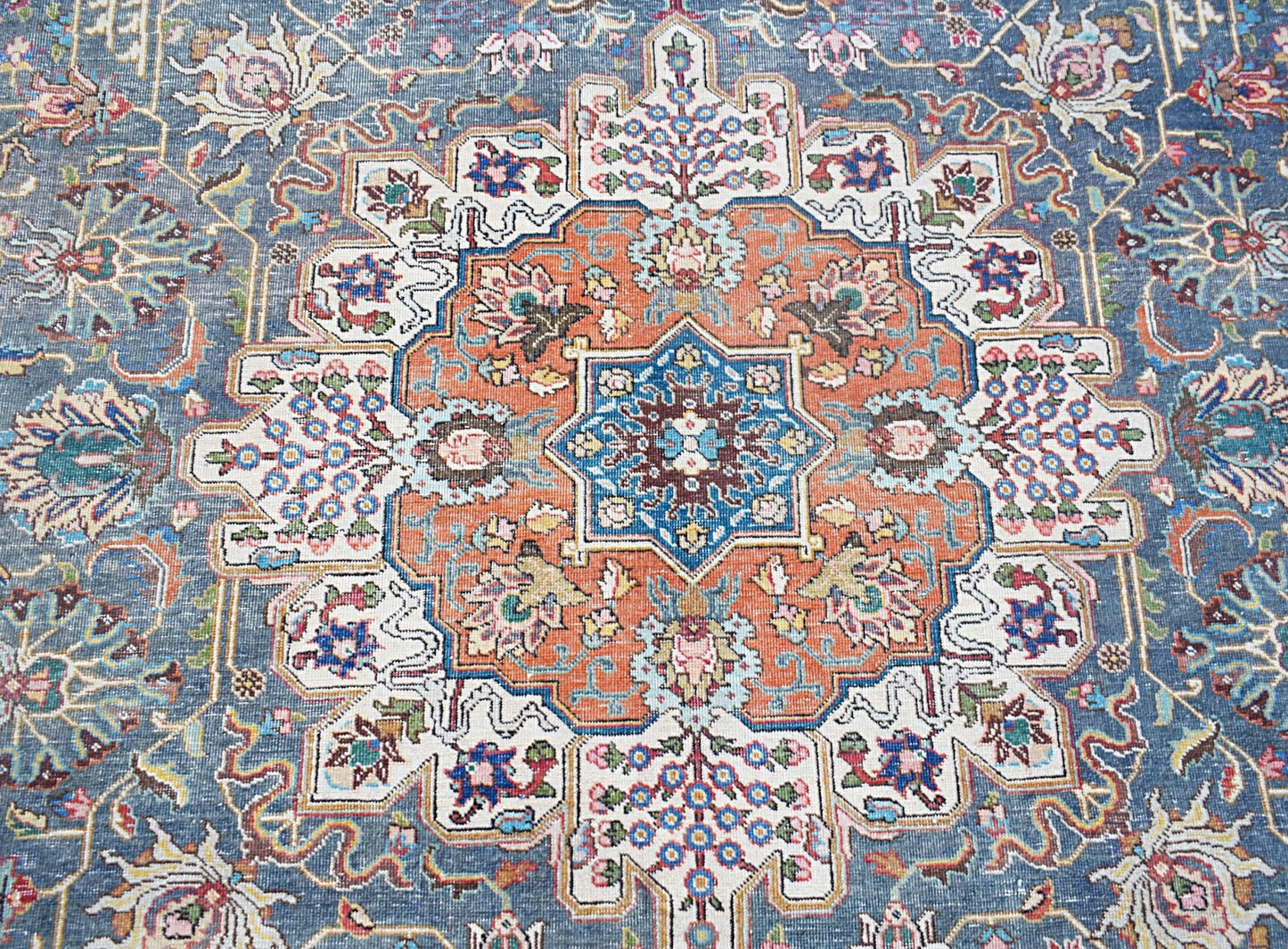 A vintage Persian Tabriz rug featuring a central floral medallion in orange and blue tones.