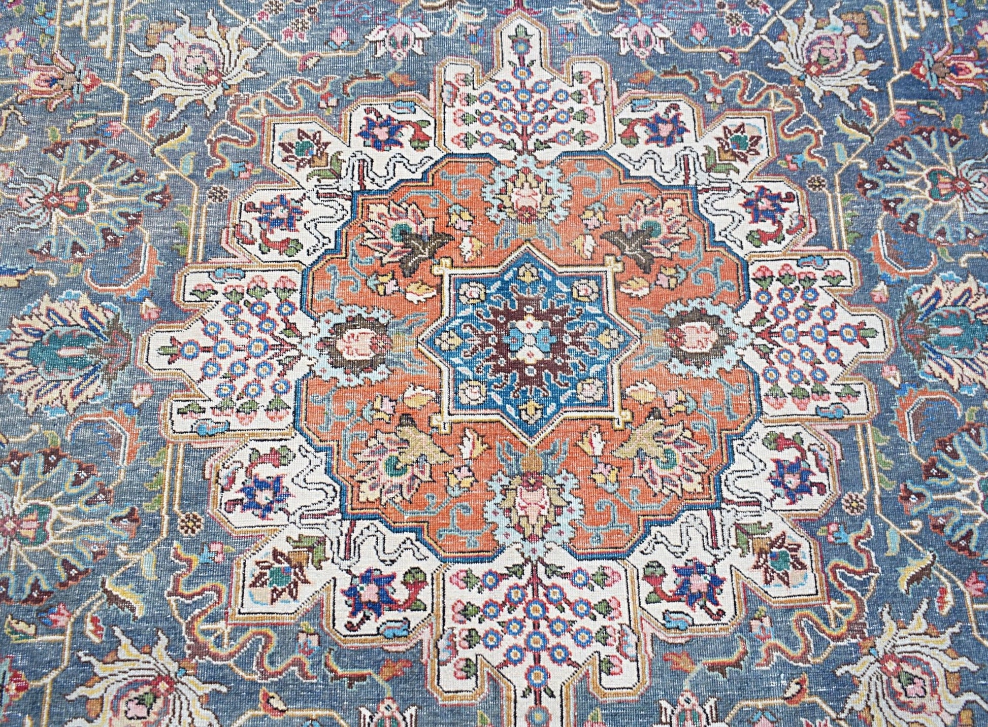 A vintage Persian Tabriz rug featuring a central floral medallion in orange and blue tones.