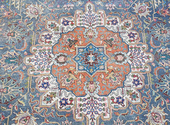 A vintage Persian Tabriz rug featuring a central floral medallion in orange and blue tones.