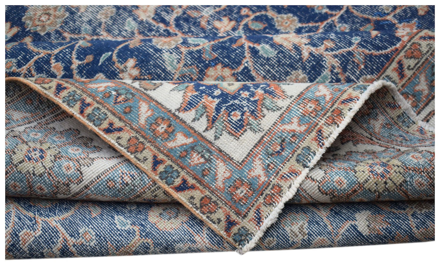 A vintage Persian Tabriz rug featuring a blue and cream floral pattern with a folded corner.