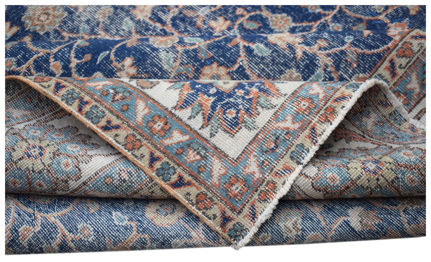 A vintage Persian Tabriz rug featuring a blue and cream floral pattern with a folded corner.