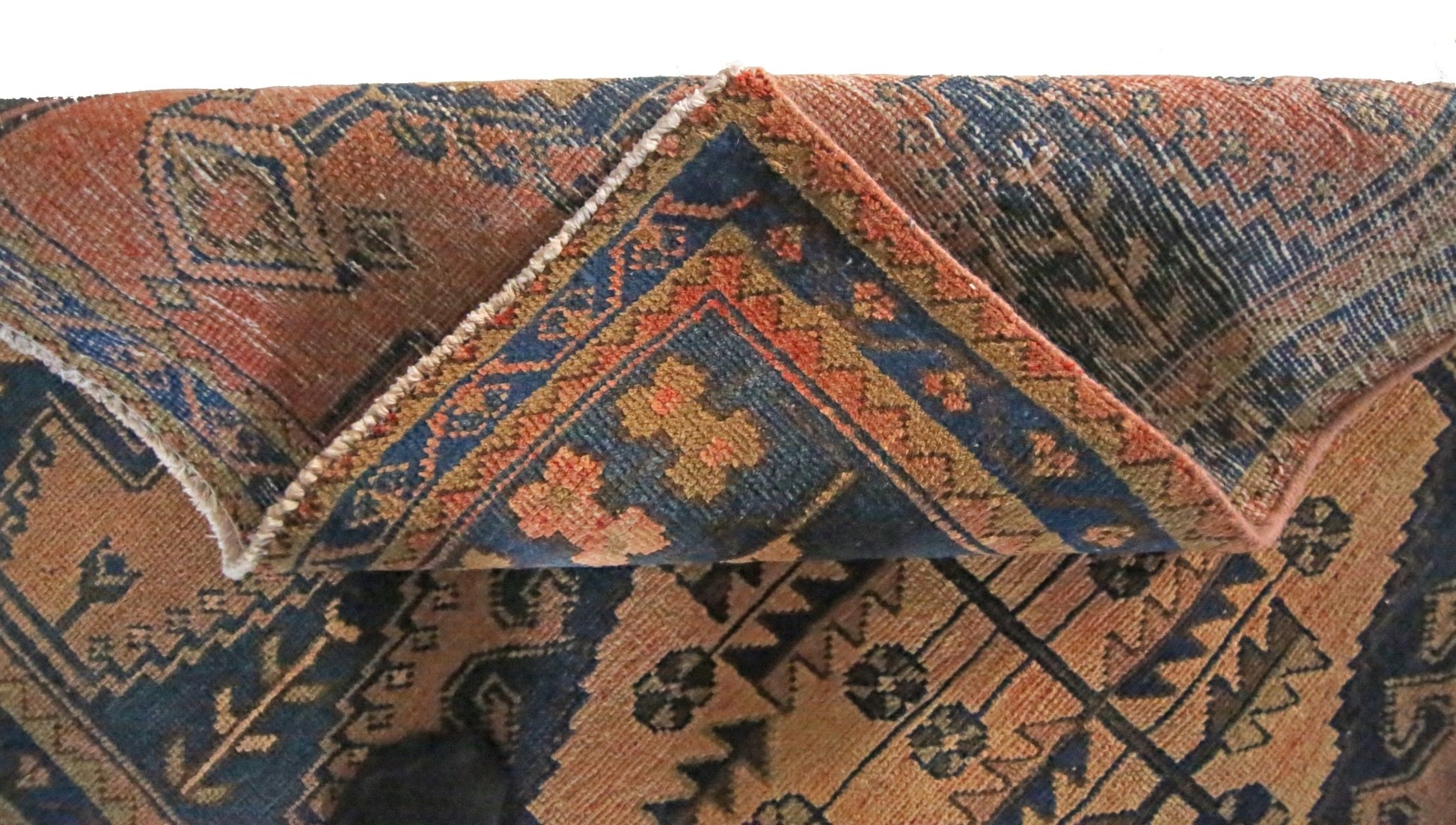 A corner of a vintage Persian Wiss rug is folded back to reveal its wool pile and cotton base.