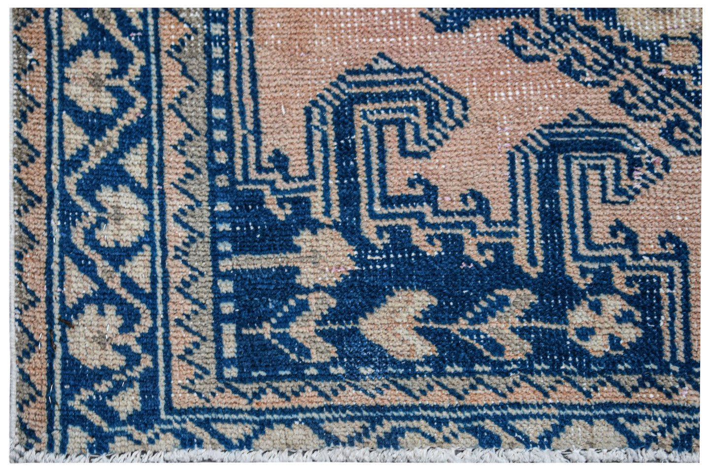 A close-up of a vintage Persian Wiss rug featuring intricate blue geometric patterns on a peach base.