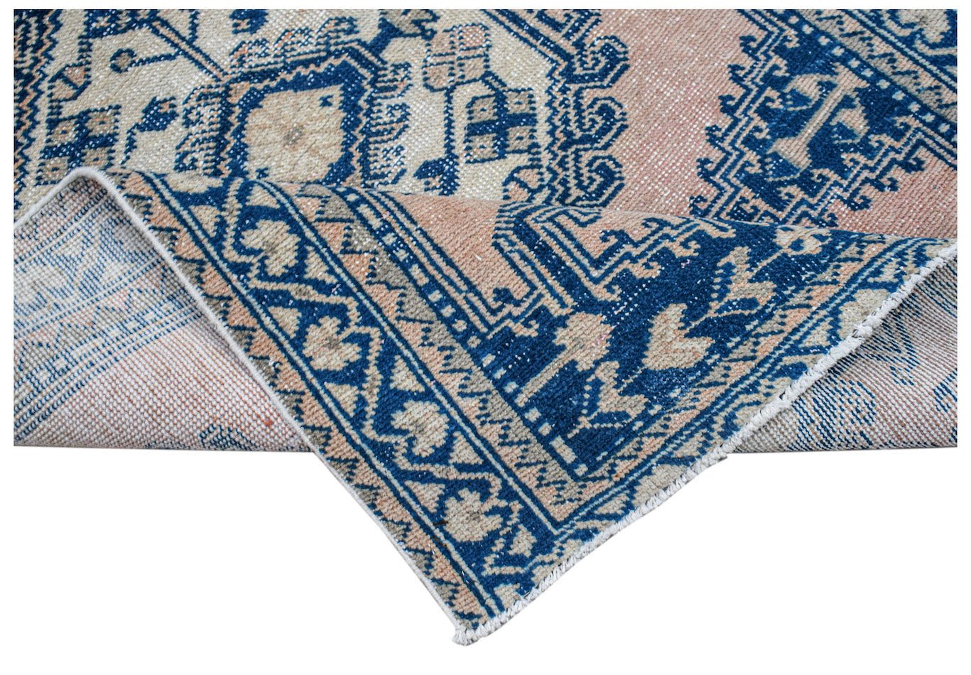 A vintage Persian rug featuring a blue and peach geometric pattern with a folded corner.
