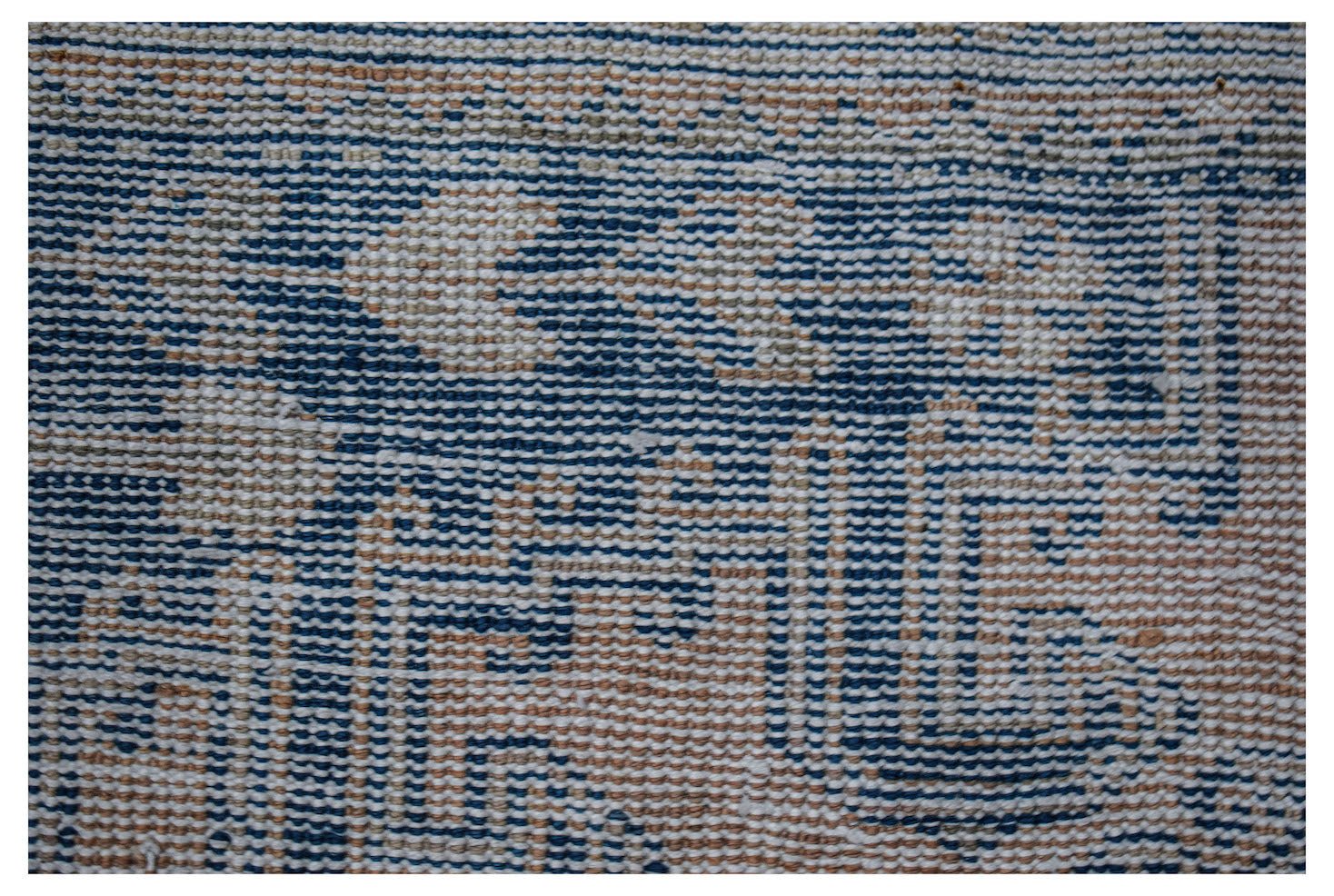 A close-up of a vintage Persian wool rug featuring a faded blue and beige geometric pattern.