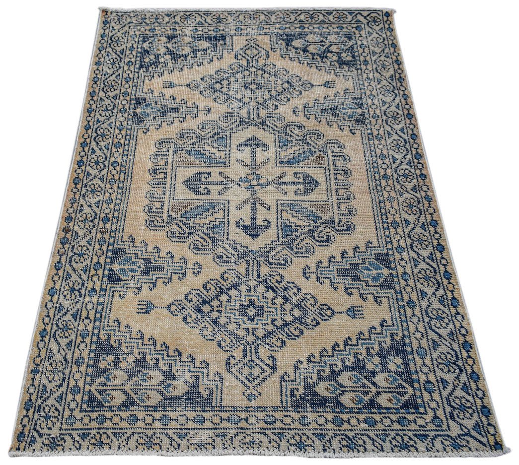 A vintage handwoven Persian rug featuring a blue geometric medallion pattern on a beige background.