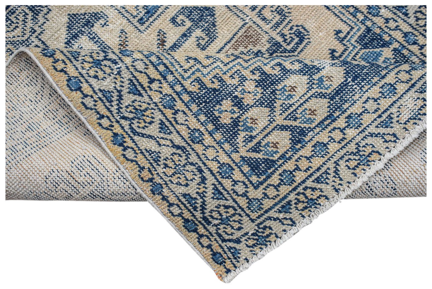 A vintage handwoven Persian rug featuring a blue and beige geometric pattern with a folded corner.