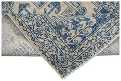 A vintage handwoven Persian rug featuring a blue and beige geometric pattern with a folded corner.