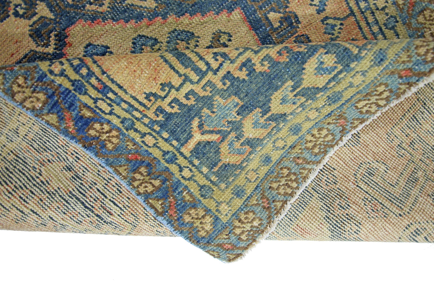 A corner of a vintage Persian Wiss rug is folded over to show its blue and tan patterned design.