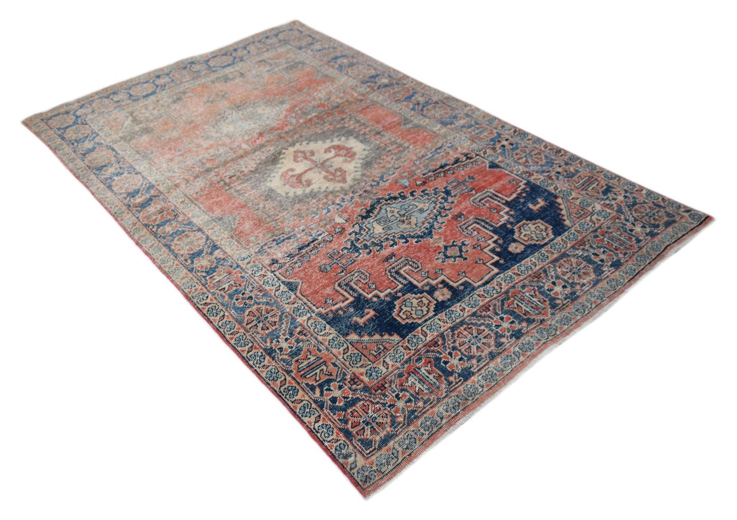 A vintage handwoven Persian wool rug featuring a distressed red and blue geometric pattern.