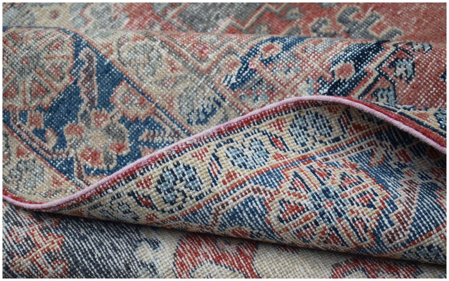 A folded vintage Persian Wiss rug featuring a traditional geometric pattern in blue and red tones.