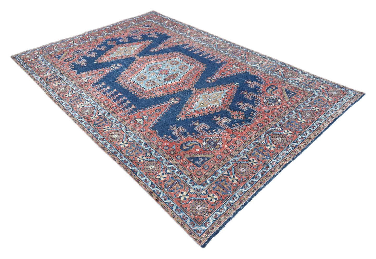 A vintage handwoven Persian rug featuring a central medallion pattern in blue and terracotta tones.