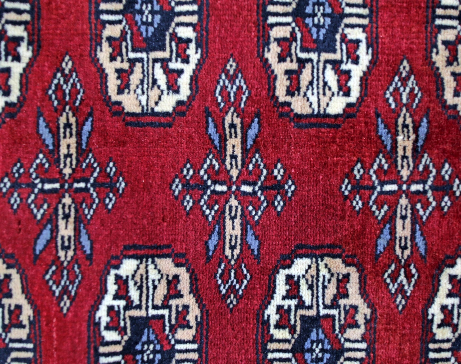 A vintage Pakistani Princess Bokhara rug featuring a repeating geometric pattern on a red background.