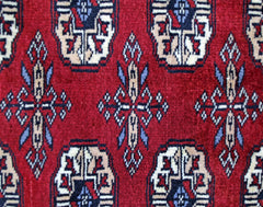 A vintage Pakistani Princess Bokhara rug featuring a repeating geometric pattern on a red background.