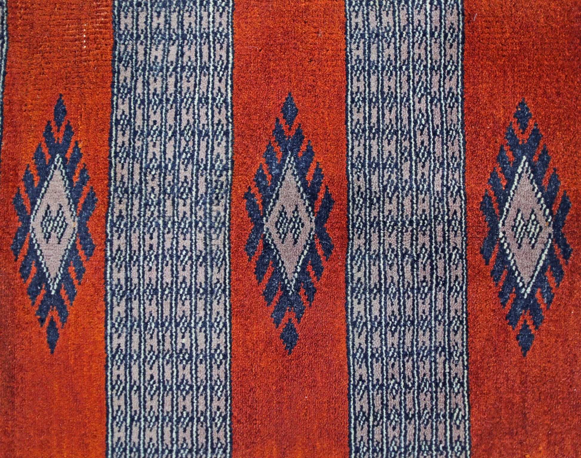 A vintage Pakistani Princess Bokhara rug featuring a repeating diamond pattern on a red background.