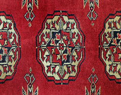 A vintage Pakistani Princess Bokhara rug featuring a repeating geometric pattern in red, cream, and black.