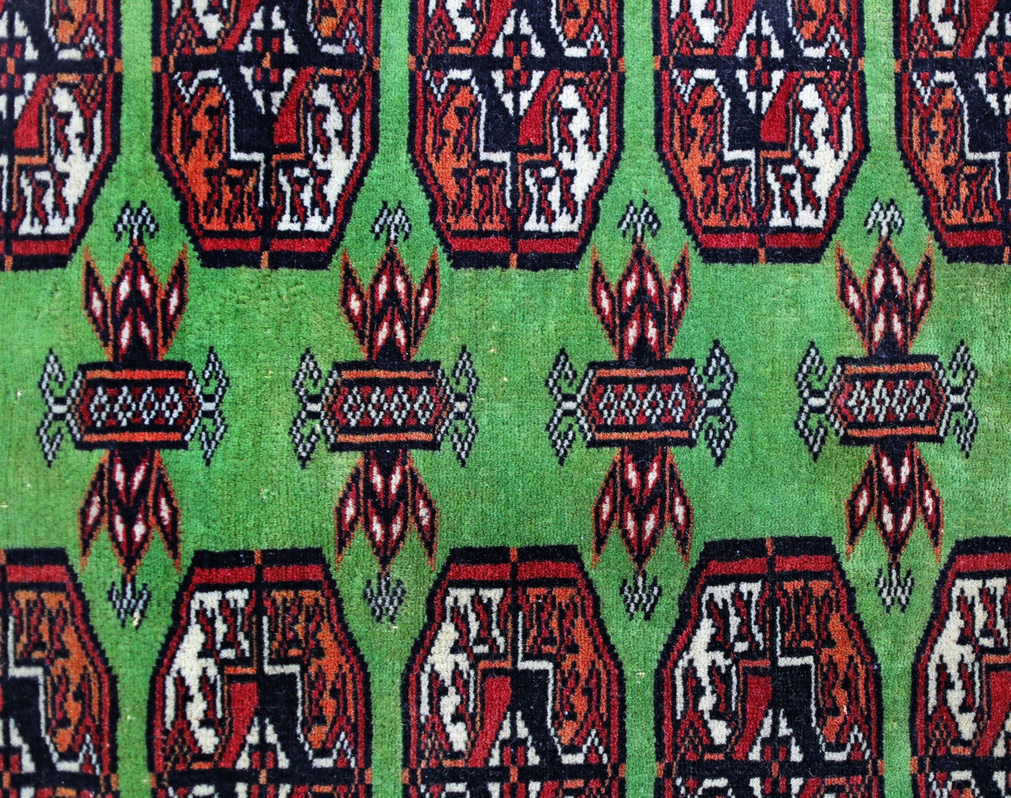 A vintage Pakistani Princess Bokhara rug featuring a repeating geometric pattern on a green field.