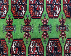 A vintage Pakistani Princess Bokhara rug featuring a repeating geometric pattern on a green field.