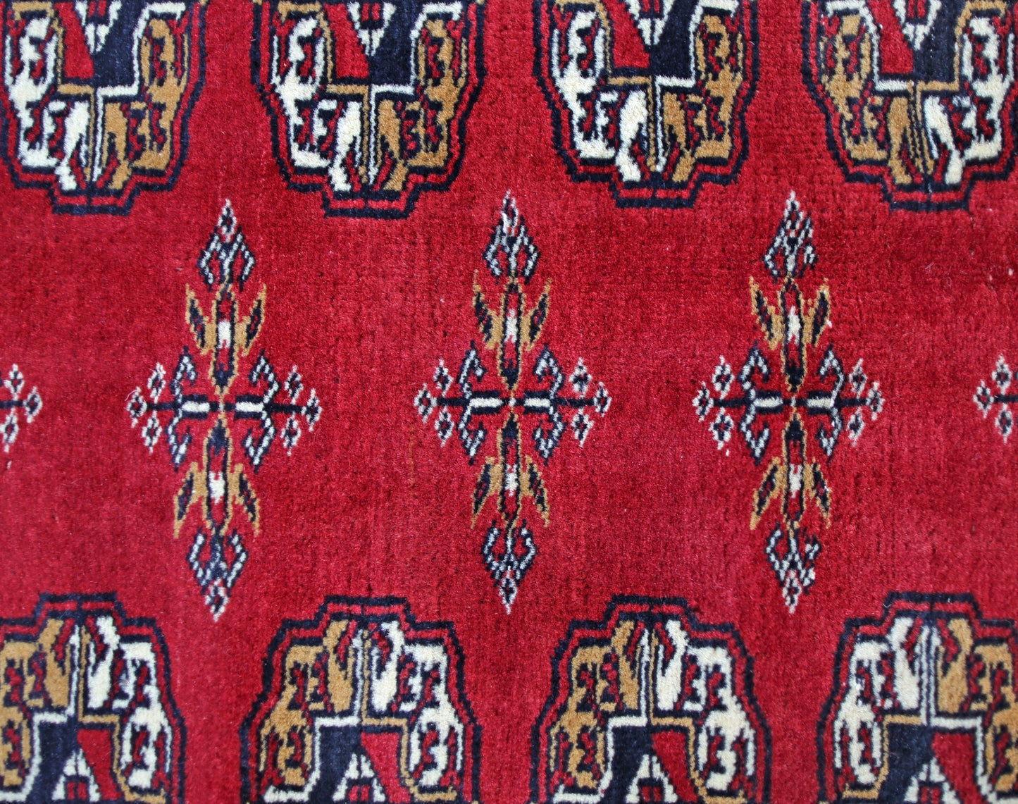 A vintage Pakistani Princess Bokhara rug featuring a repeating geometric pattern on a red field.